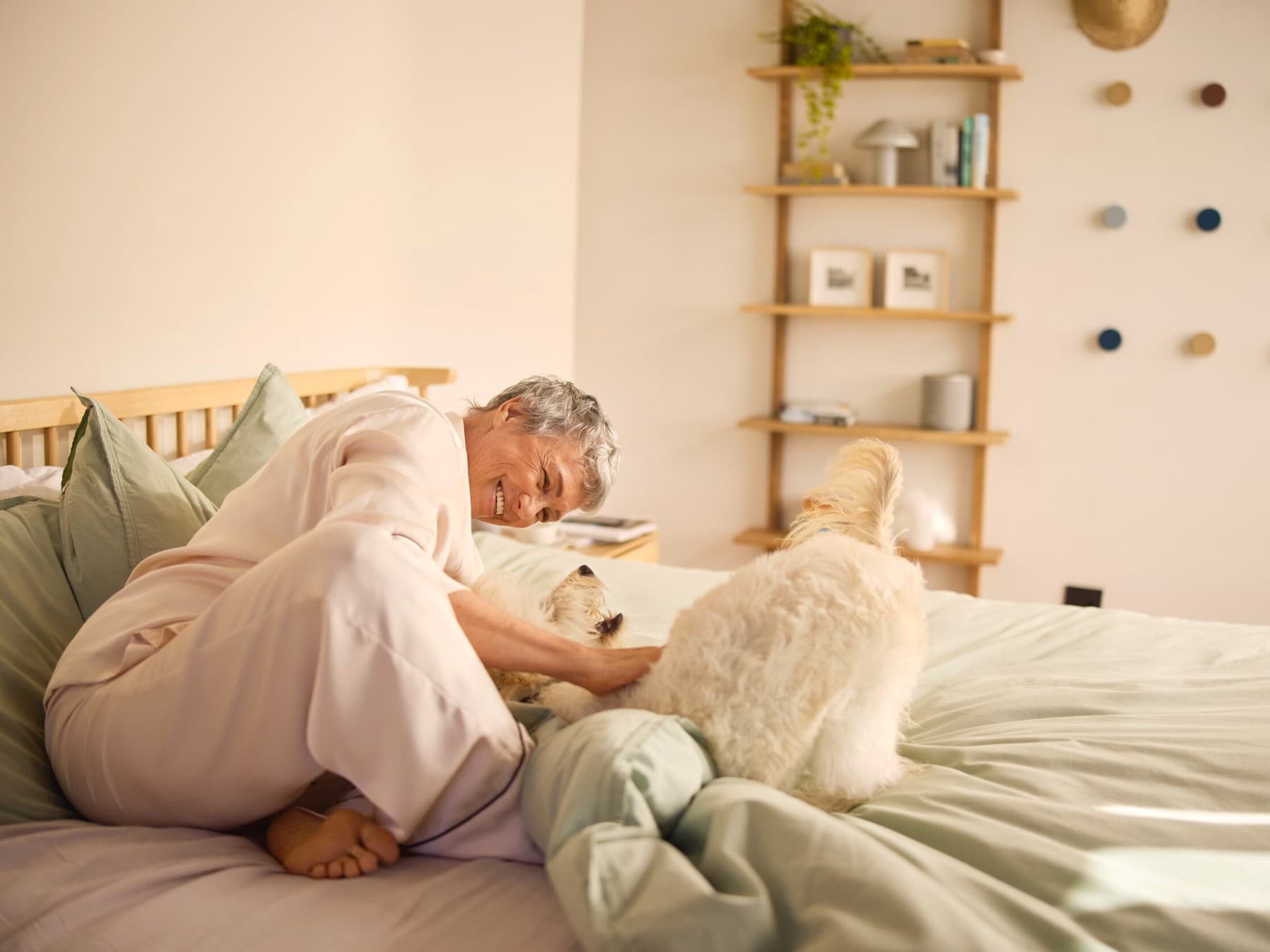 Een glimlachende vrouw die een hond op een bed aait