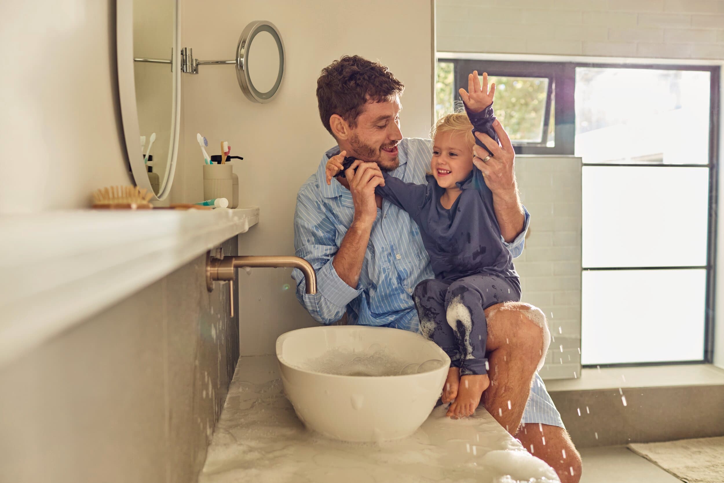 Vader en kind zitten naast een wastafel.
