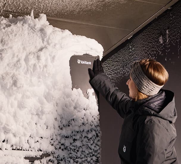 Vrouw staat voor een met sneeuw bedekte warmtepomp.