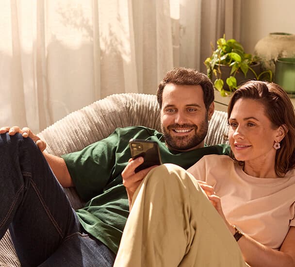 Een stel zit op de bank en kijkt op een mobiele telefoon.