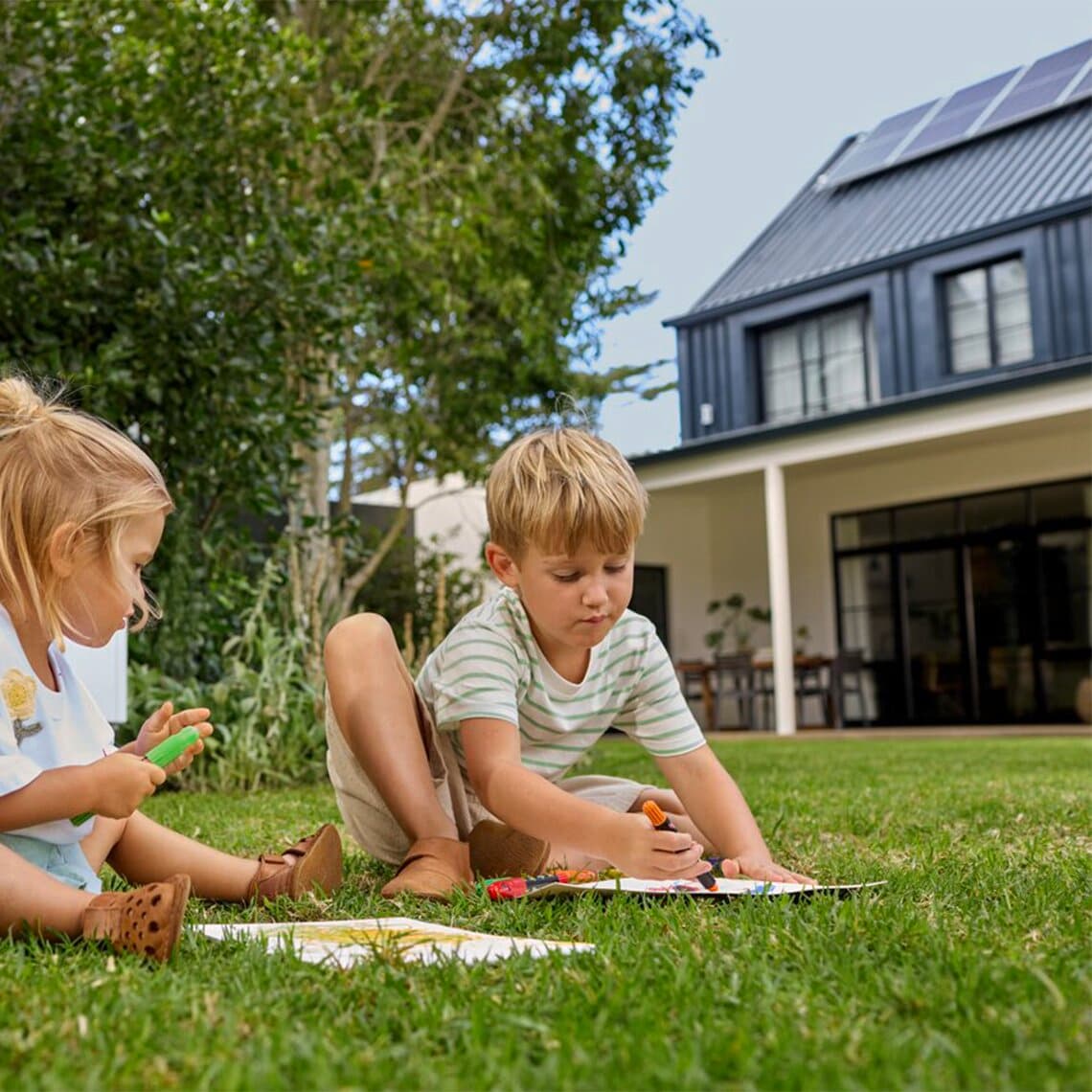 Kinderen spelen in de tuin van een huis met zonnepanelen op het dak