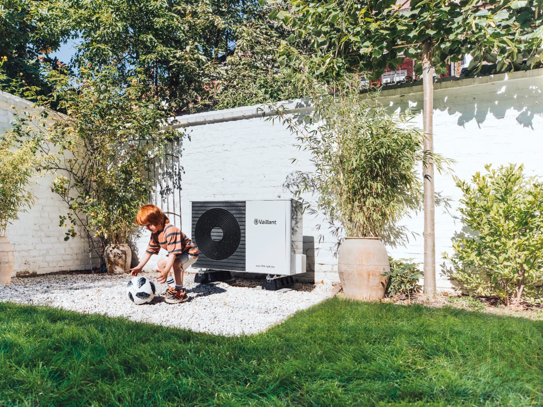 Kind dat voetbalt in de tuin voor een warmtepomp