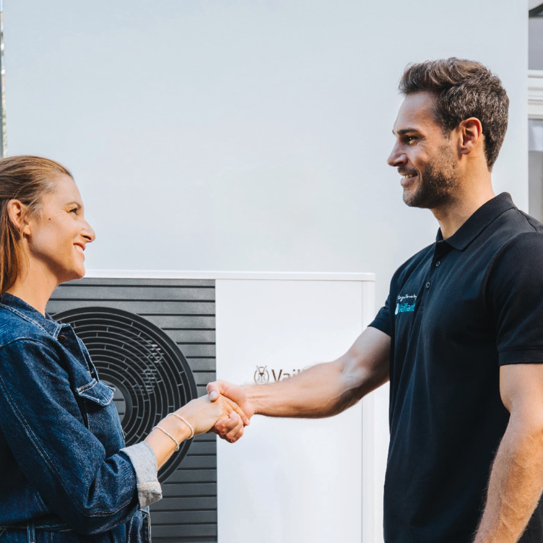 Een installateur en een vrouw die elkaar de hand schudden voor een warmtepomp
