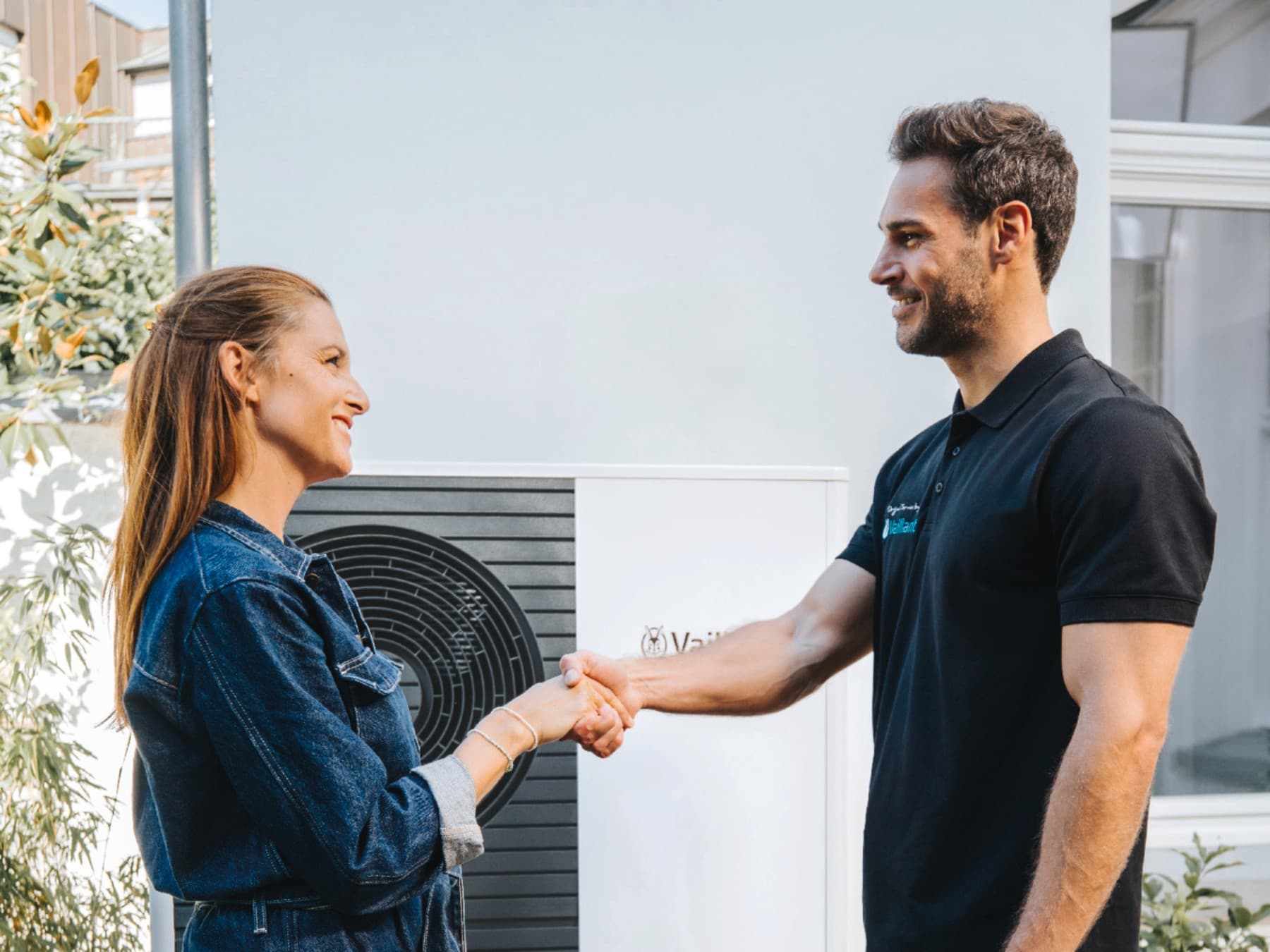 Vrouw en Vaillant-medewerker schudden elkaar de hand voor een warmtepomp.