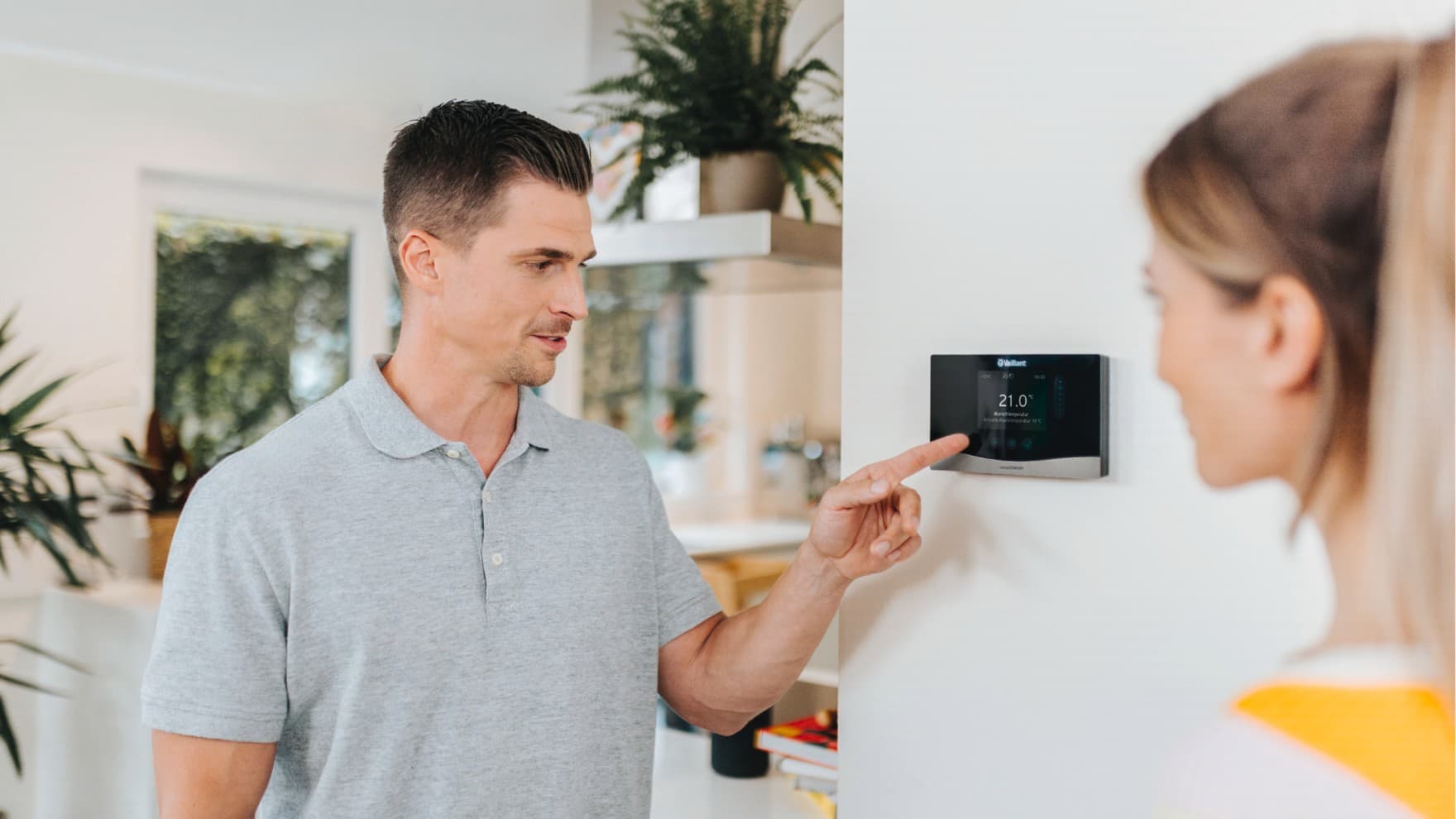Op de voorgrond staat een man met zijn hand op een verwarmingsknop die op een blauwe muur is bevestigd.