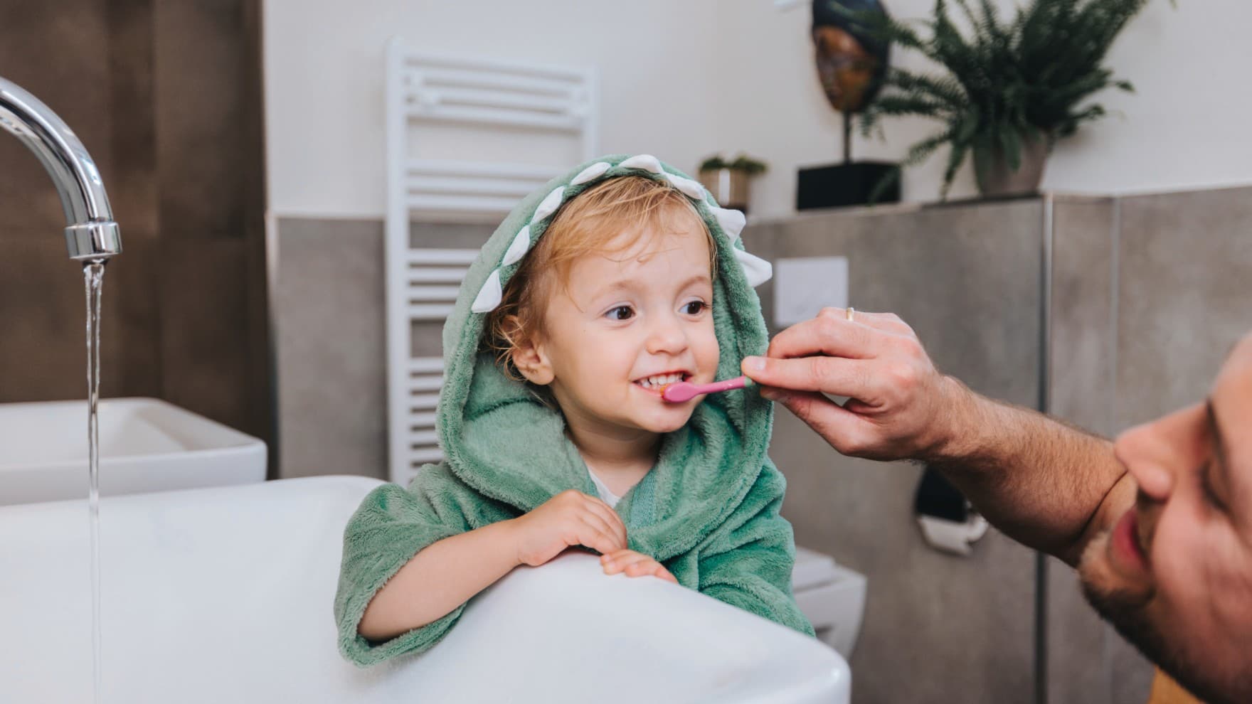 Vader poetst de tanden van zijn kind met een verwarmde handdoekhouder op de achtergrond.