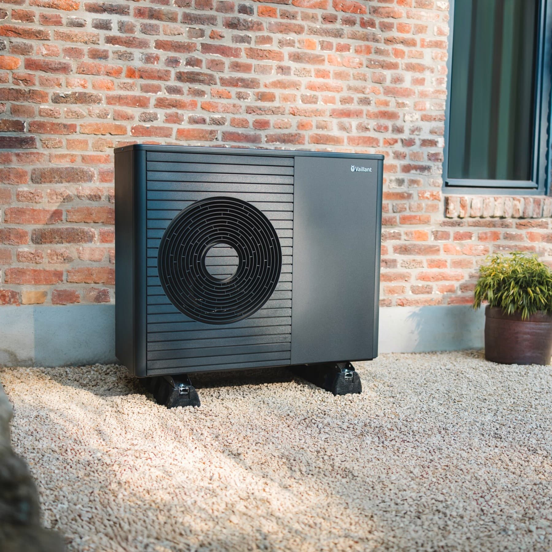 Een warmtepomp staat voor een nieuw gebouw en een pad op de voorgrond.