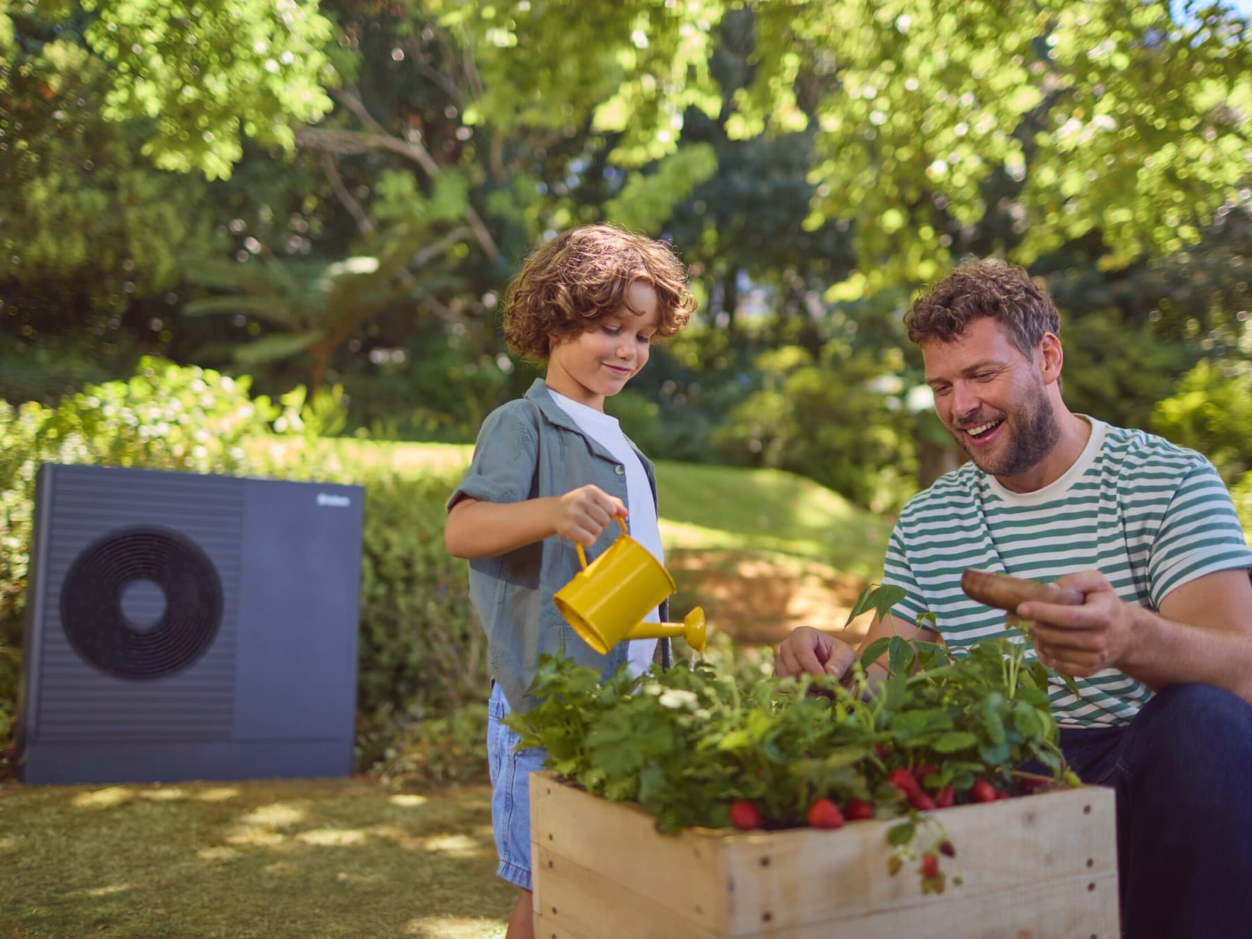 Man met zijn zoon aan het tuinieren. Buitenunit van een warmtepomp in de tuin