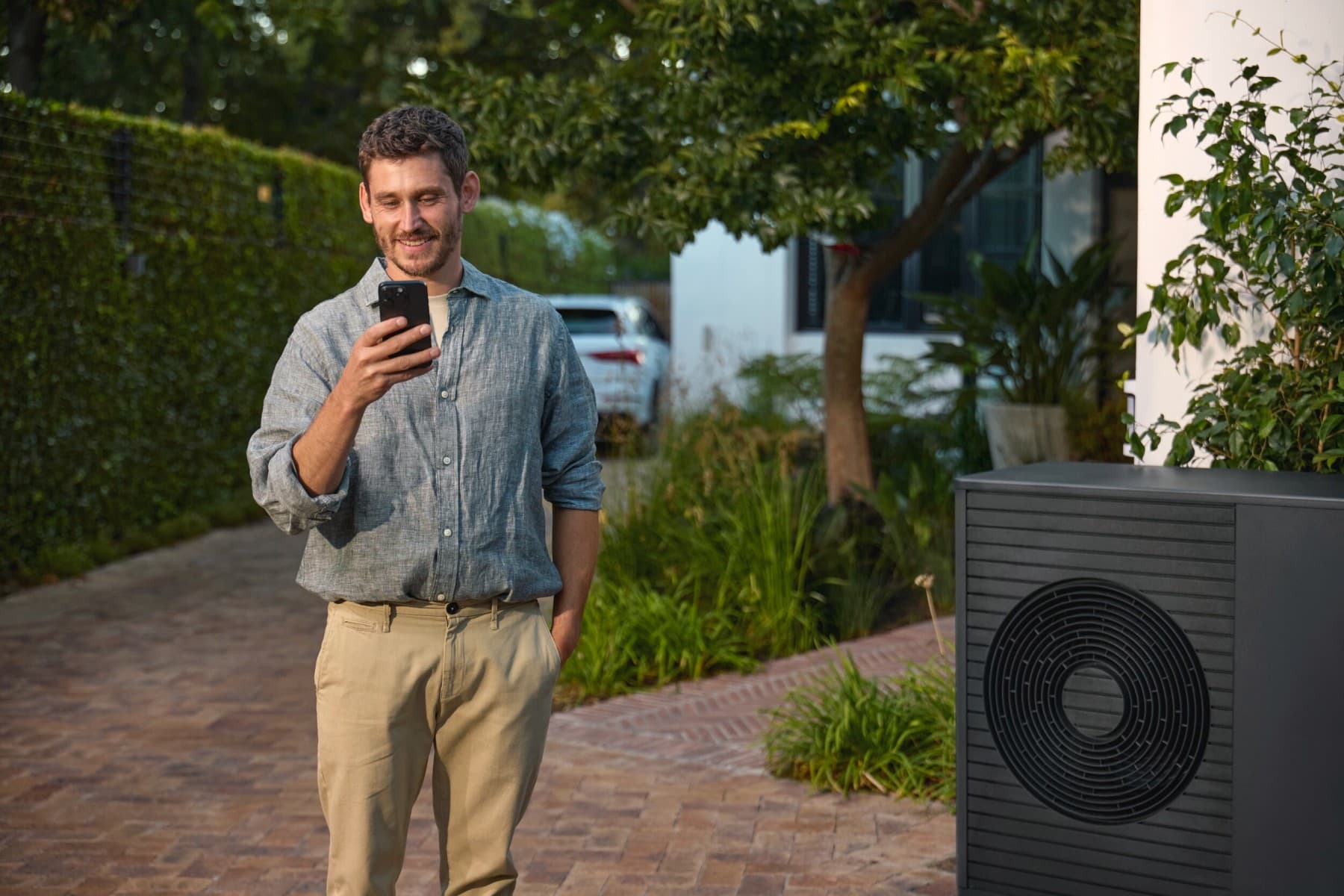 Man die naast een warmtepomp staat en naar een smartphone kijkt