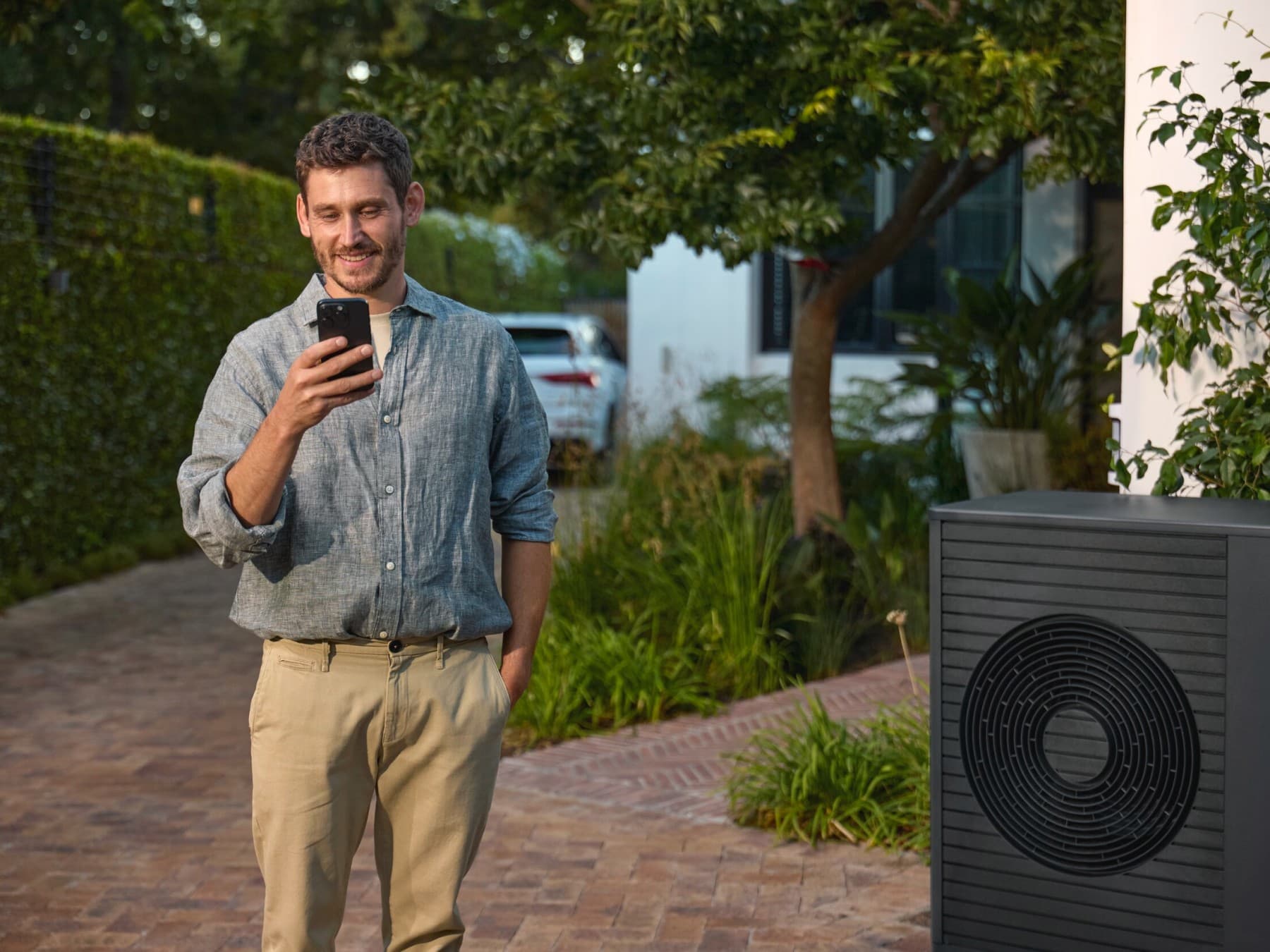 Man die naast een warmtepomp staat en naar een smartphone kijkt