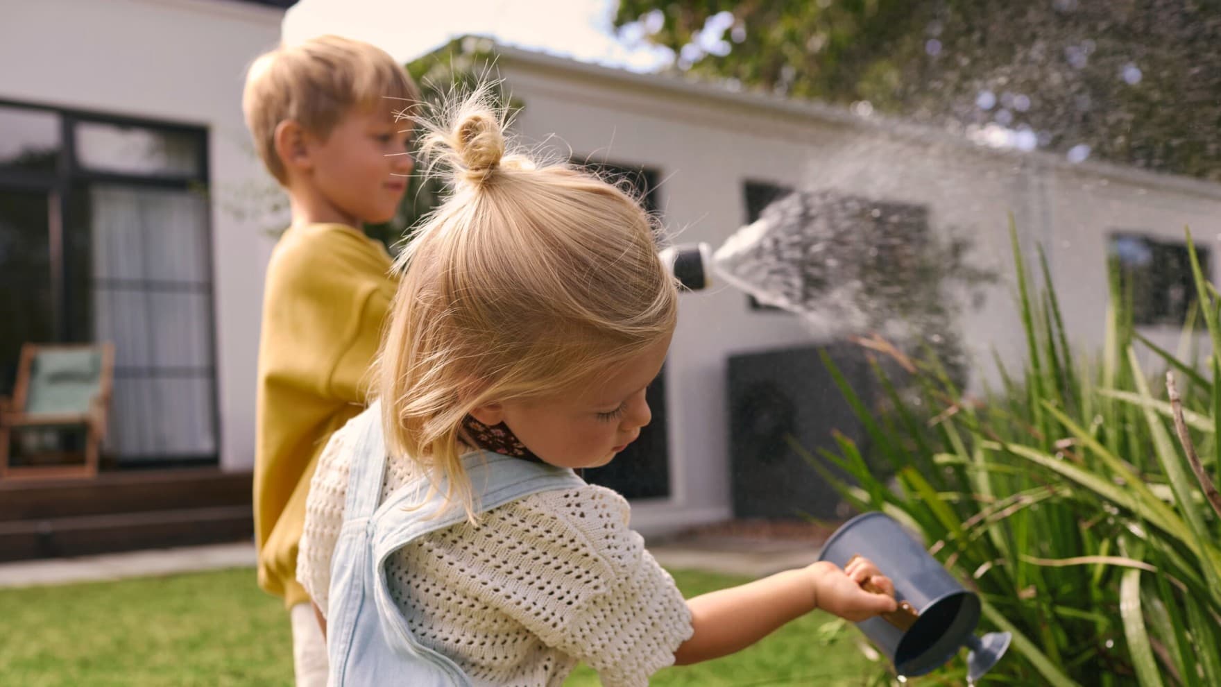 Kinderen geven planten water in een tuin met een warmtepomp op de achtergrond.