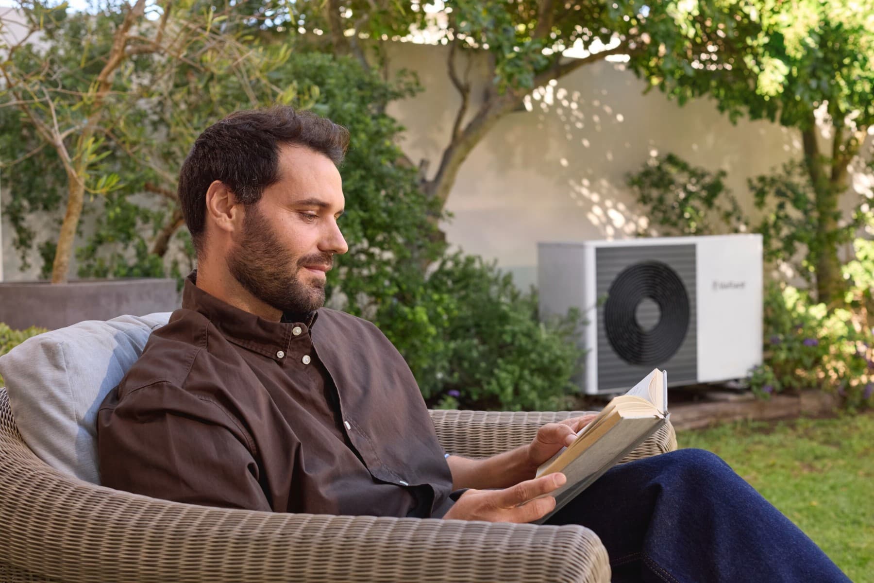 Een man zit in een tuin voor een warmtepomp.
