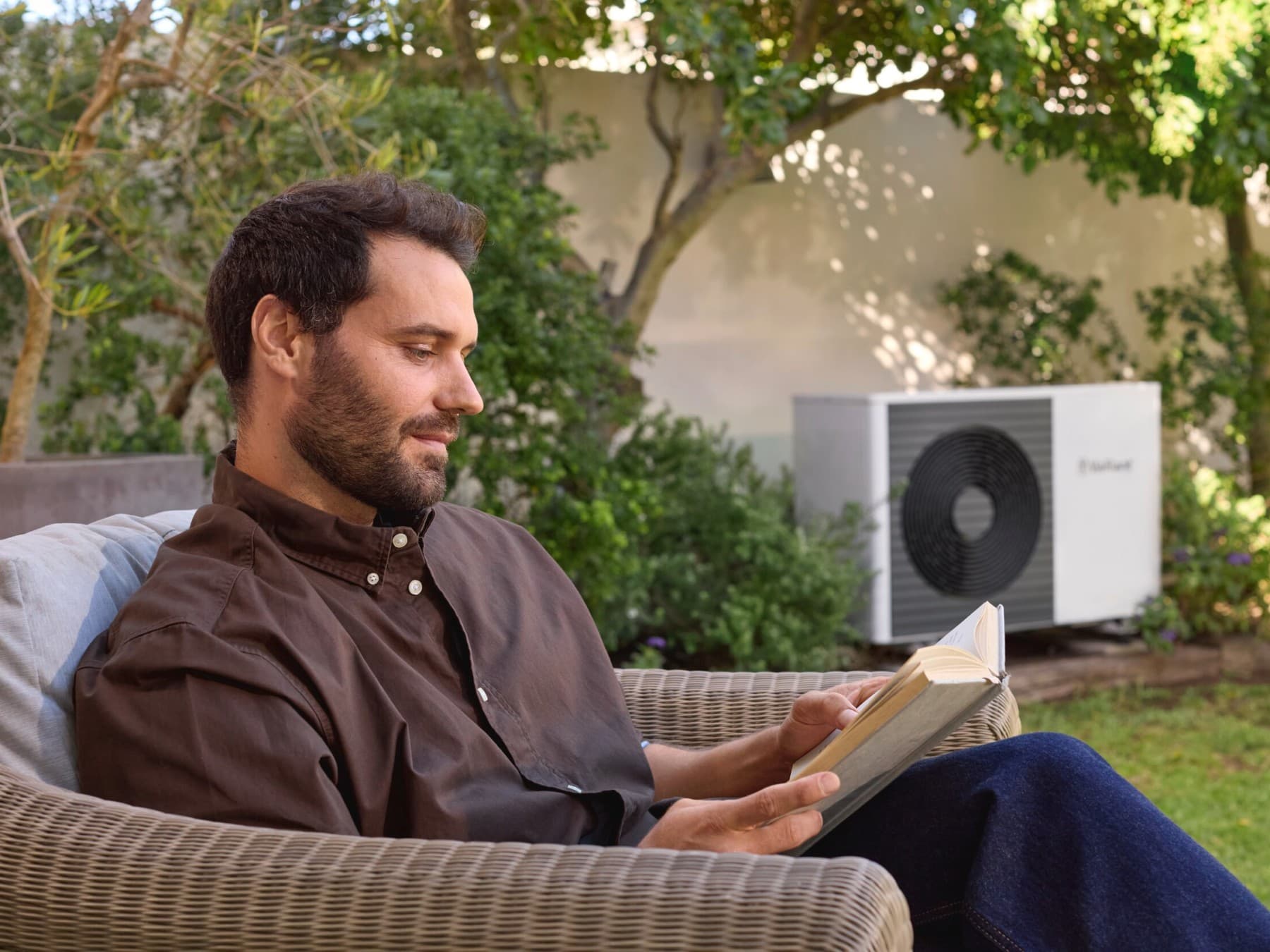 Warmtepomp buitenunit in een tuin met de eigenaar ernaast zittend